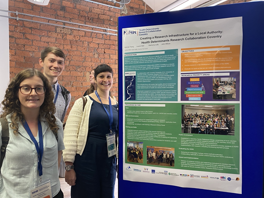 Picture of Lauren Bell, Cameron Ley, Valerie De Souza (left to right), standing in front of a poster abstract that details the process of creating a research infrastructure for the local authority: Health Determinants Research Collaboration Coventry City