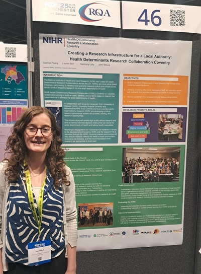 An image of Research Fellow Lauren Bell in front of a poster abstract that details the process of creating a research infrastructure for the local authority: Health Determinants Research Collaboration Coventry City Council.